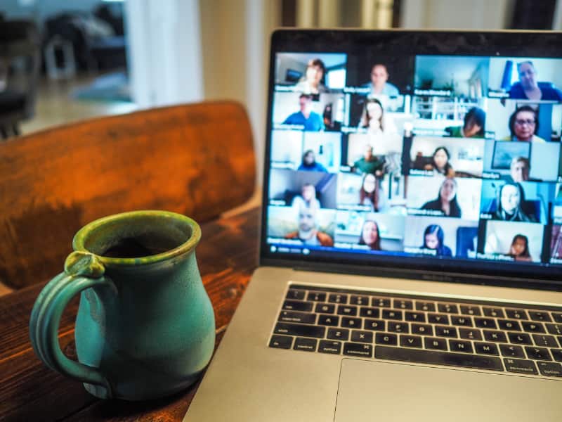 Mug beside laptop with zoom meeting on screen with many people participating